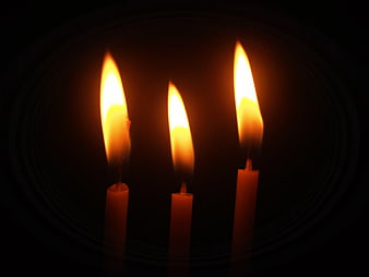 Three lit candles glowing in the dark