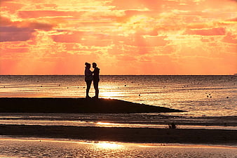 Silhouetted couple standing on a sandbar during a vibrant orange sunset