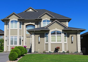 Modern beige two-story house with green lawn and blue sky