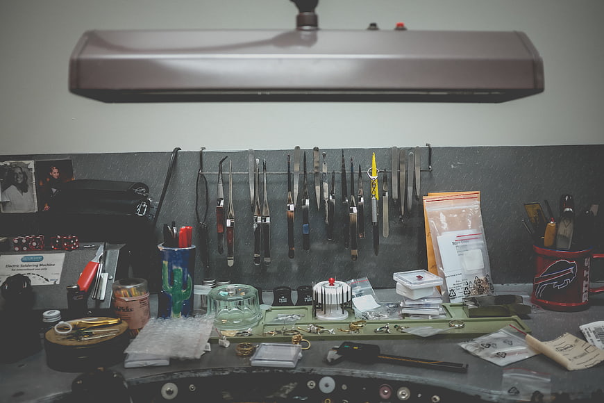 Cluttered jewelry making workspace with tools and lamp