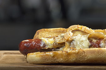 Close-up of a grilled sausage in a toasted bun with melted cheese and onions