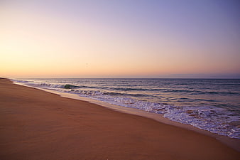 Empty sandy beach with gentle waves and pastel sunrise sky