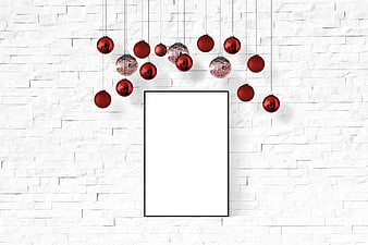 Christmas baubles hanging above blank poster frame on white brick wall