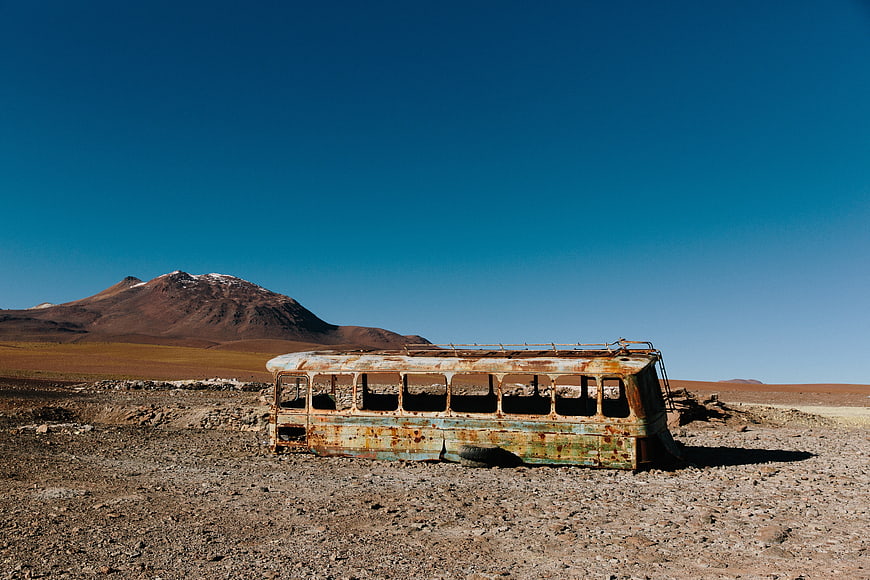 Rusty abandoned bus in desert landscape with mountains