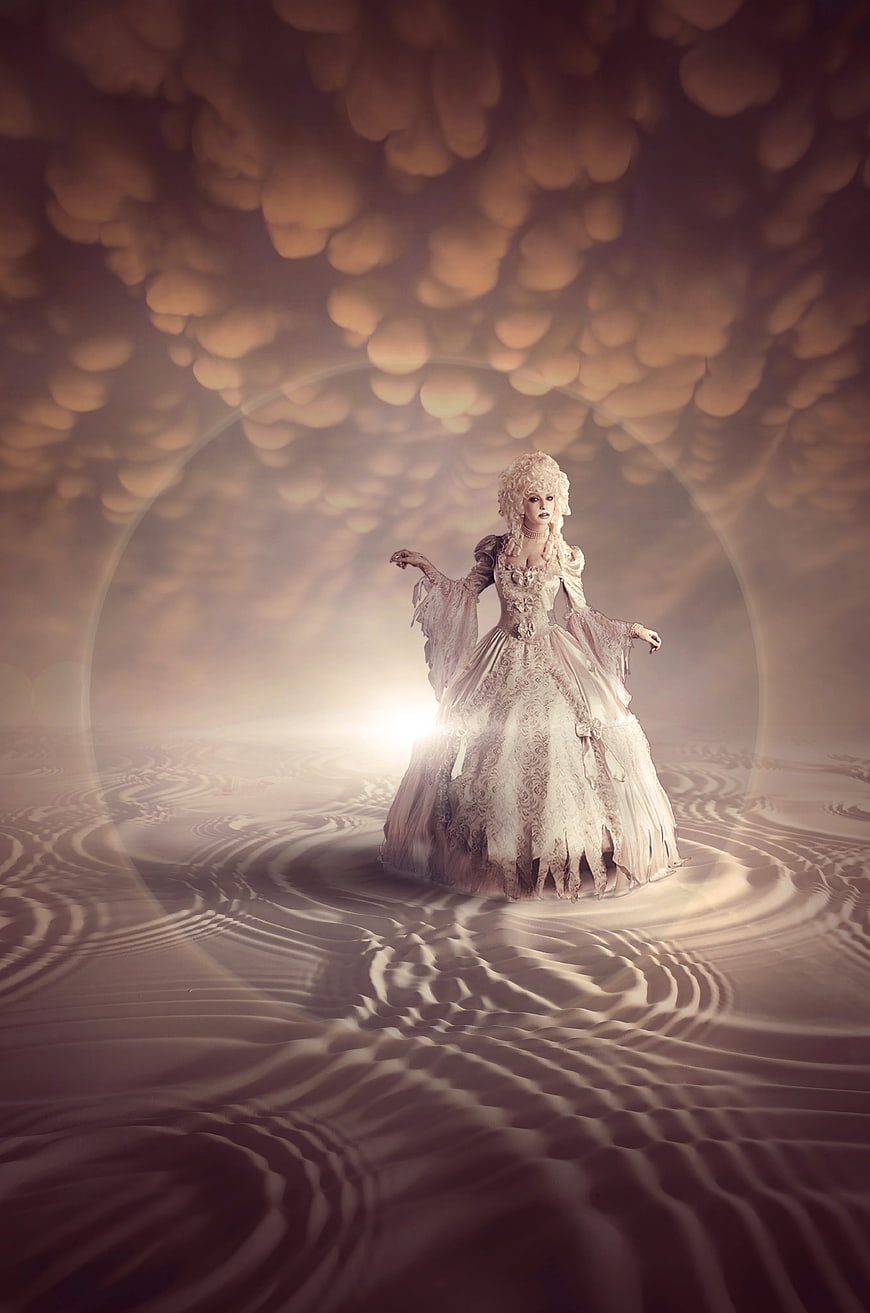 Mystical woman in baroque gown standing in surreal desert landscape