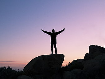 Silhouette of Man Standing on Rock with Arms Raised at Sunset