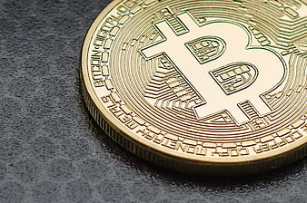 Close-up of a gold Bitcoin coin on a dark textured surface