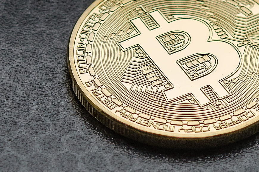 Close-up of a gold Bitcoin coin on a dark textured surface