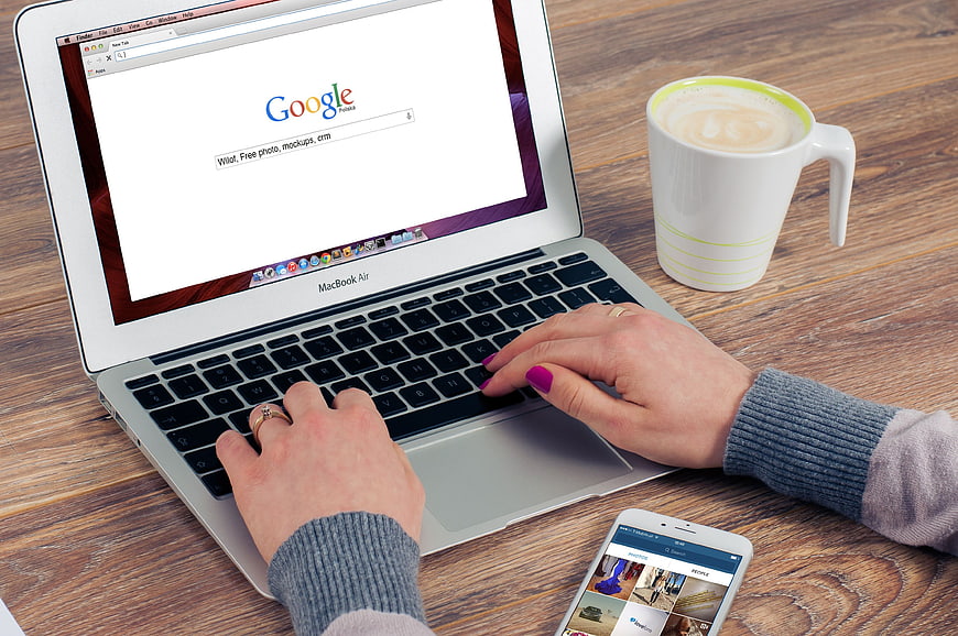 Woman Typing on MacBook Air with Coffee and Smartphone
