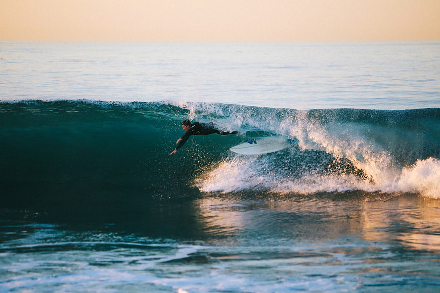 Surfer paddling on wave at golden hour ocean sunset