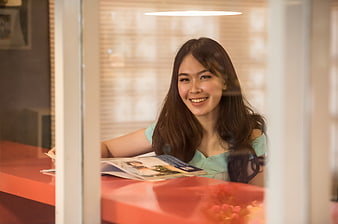 Smiling young Asian woman reading a magazine at a cafe table