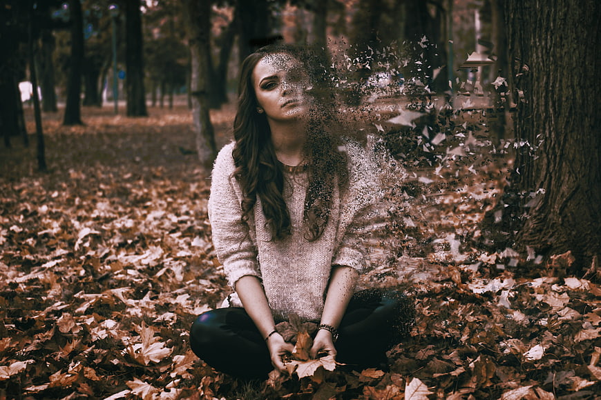 Woman dissolving into autumn leaves in forest