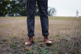 Man's brown leather boots and rolled-up jeans in a field