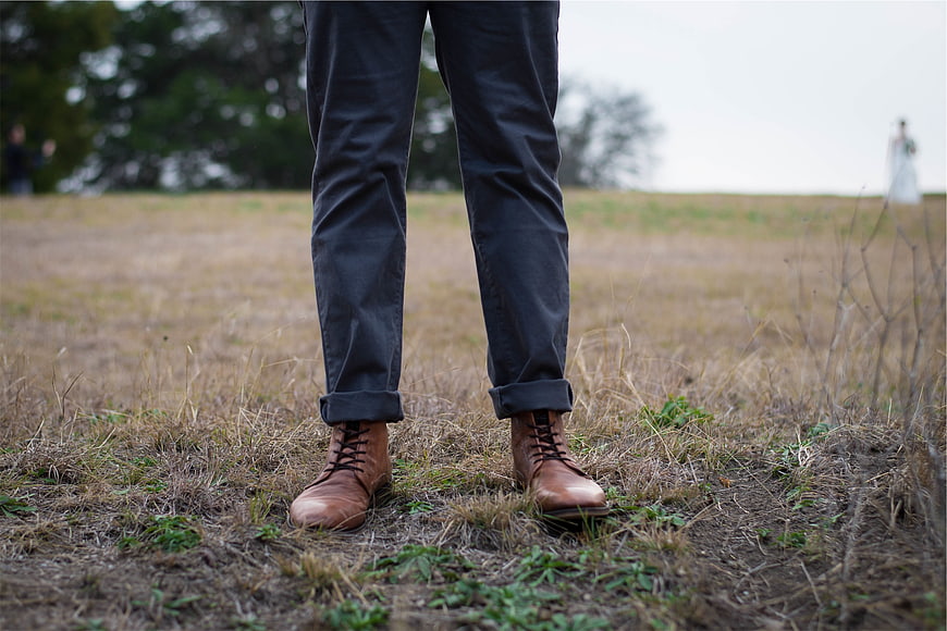 Man's brown leather boots and rolled-up jeans in a field