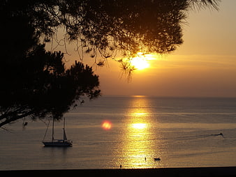 Golden sunset over calm sea with sailboat silhouette