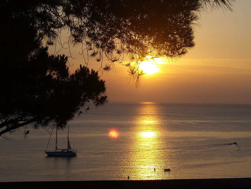 Golden sunset over calm sea with sailboat silhouette