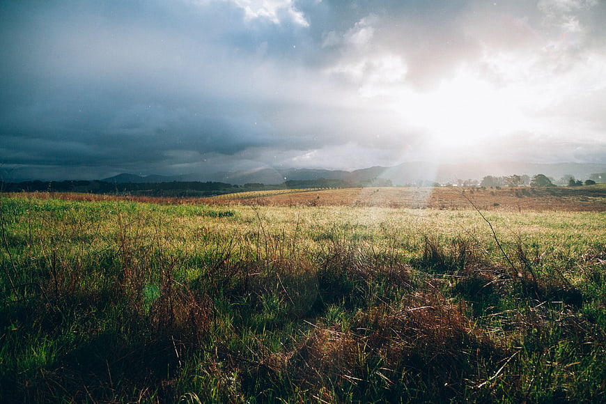 Dramatic Sunbeams Breaking Through Clouds Over Rural Grassland
