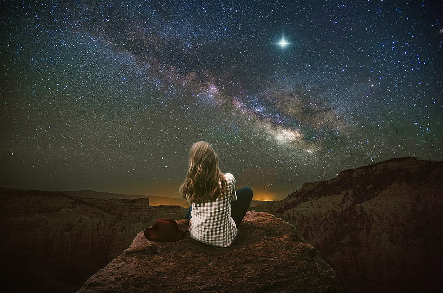 Woman Sitting On Rock Under Milky Way Night Sky