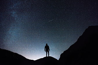 Silhouette of Man Standing on Mountain Peak Under Starry Night Sky
