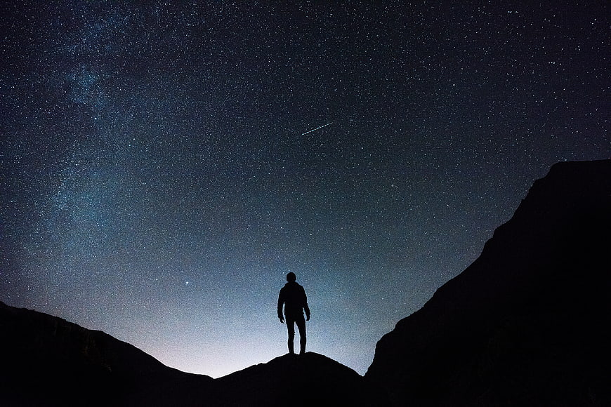 Silhouette of Man Standing on Mountain Peak Under Starry Night Sky