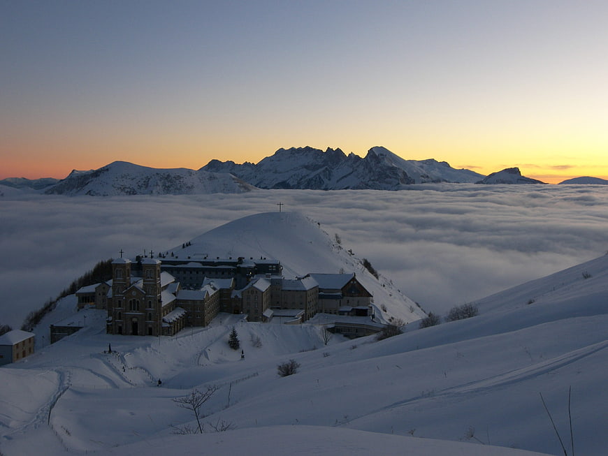 Snowy mountain monastery above sea of clouds at sunset