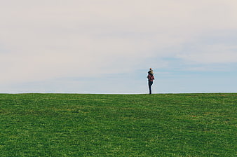 Lone figure standing on a green grassy hill against a cloudy sky