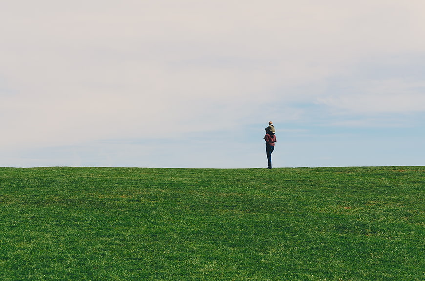 Lone figure standing on a green grassy hill against a cloudy sky