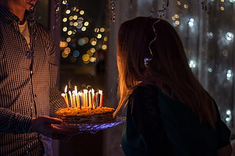 Man presenting birthday cake with lit candles to woman