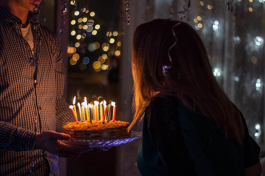 Man presenting birthday cake with lit candles to woman