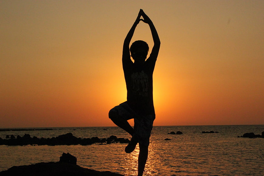 Silhouette of man doing yoga tree pose on beach at sunset