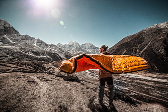 Man holding orange sleeping bag in snowy mountain landscape