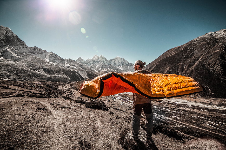 Man holding orange sleeping bag in snowy mountain landscape