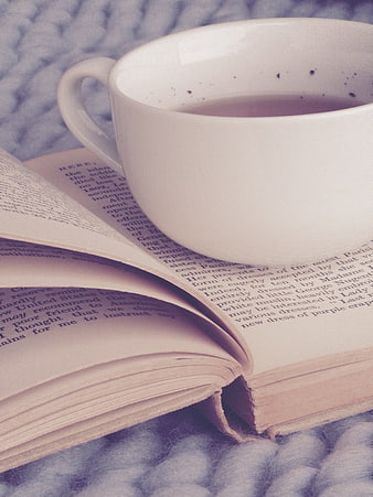 White coffee cup resting on an open book on a soft gray blanket