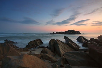 Serene Sunset Over Rocky Beach with Smooth Ocean Waves