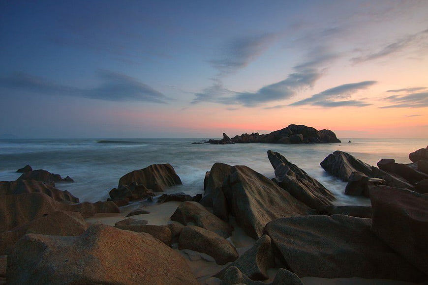 Serene Sunset Over Rocky Beach with Smooth Ocean Waves