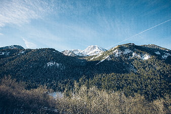 Snowy Mountain Peaks and Forested Slopes Under Blue Sky