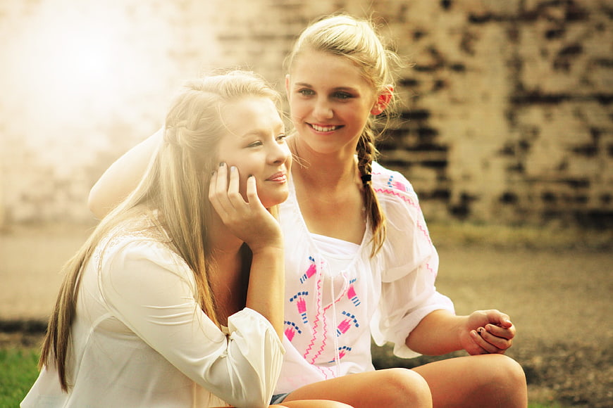 Two smiling teenage girls sitting outdoors in white blouses