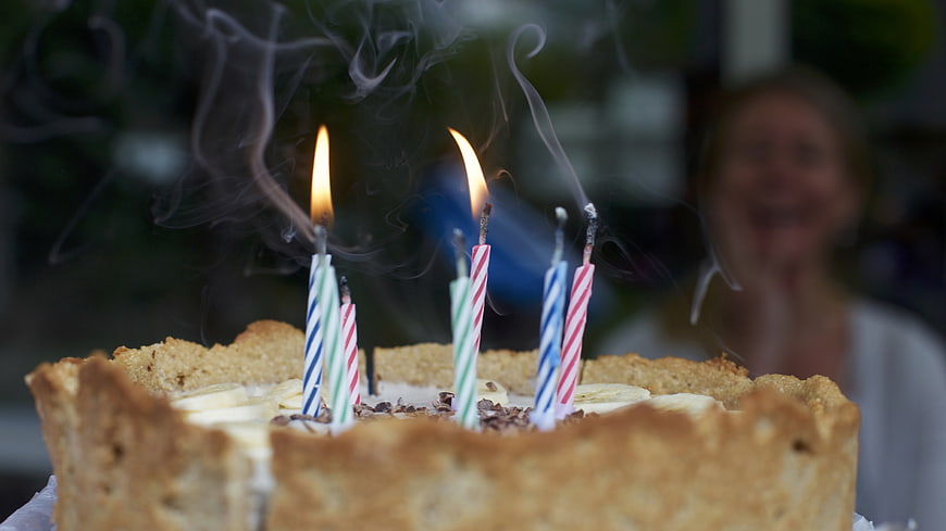 Birthday cake with lit candles and blurred smiling woman