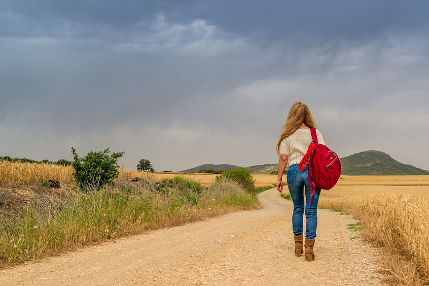 Woman with red backpack walking on rural dirt road