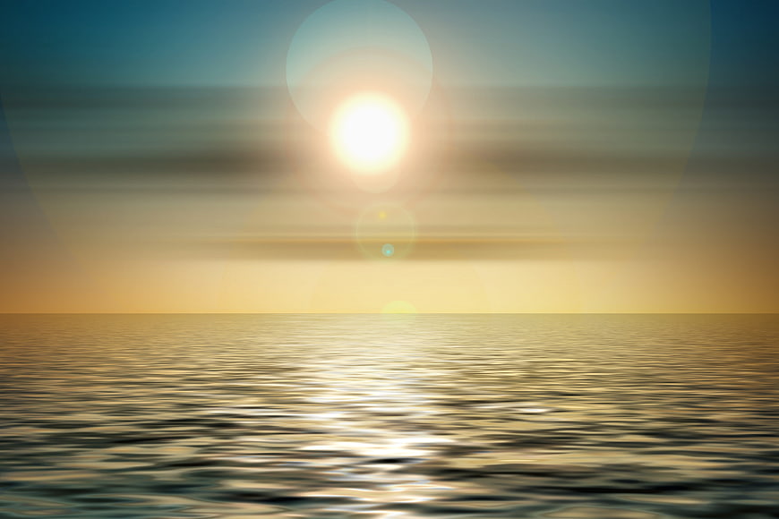Sunset over calm ocean with lens flare and golden light reflection