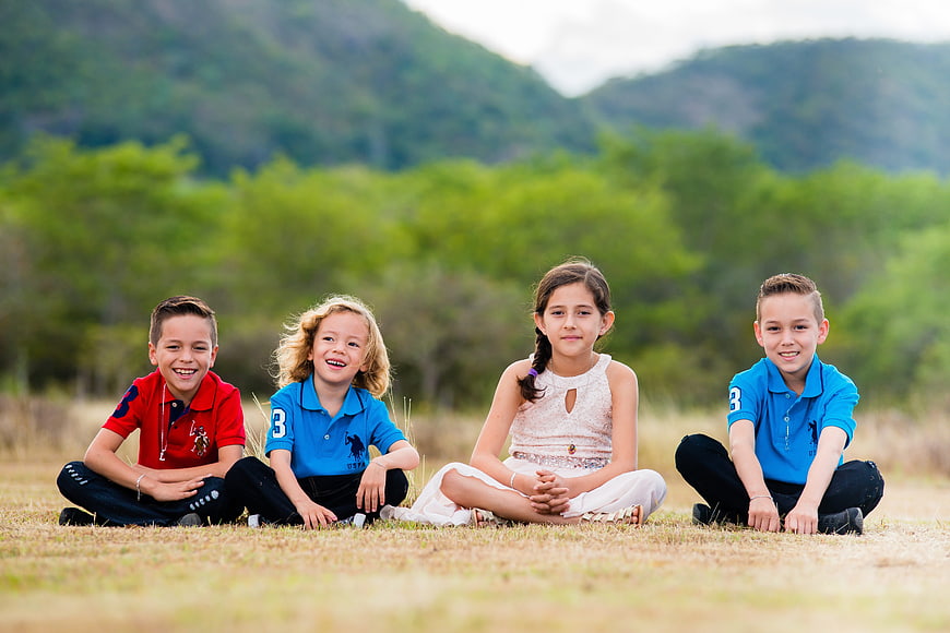 Four happy children sitting in a grassy field with mountains