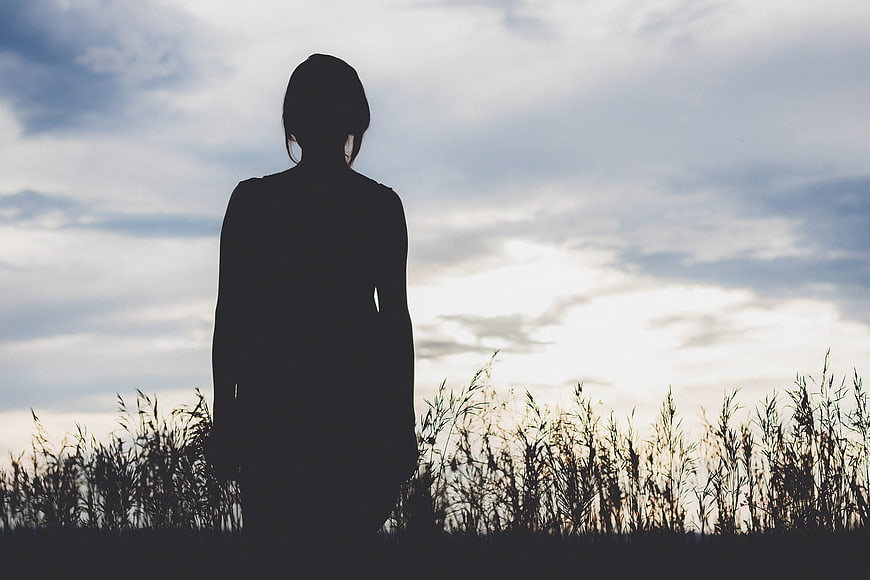 Silhouette of Woman Standing in Tall Grass Against Cloudy Sky