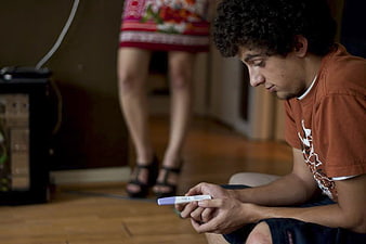 Young Man Holding Pregnancy Test with Woman Standing in Background