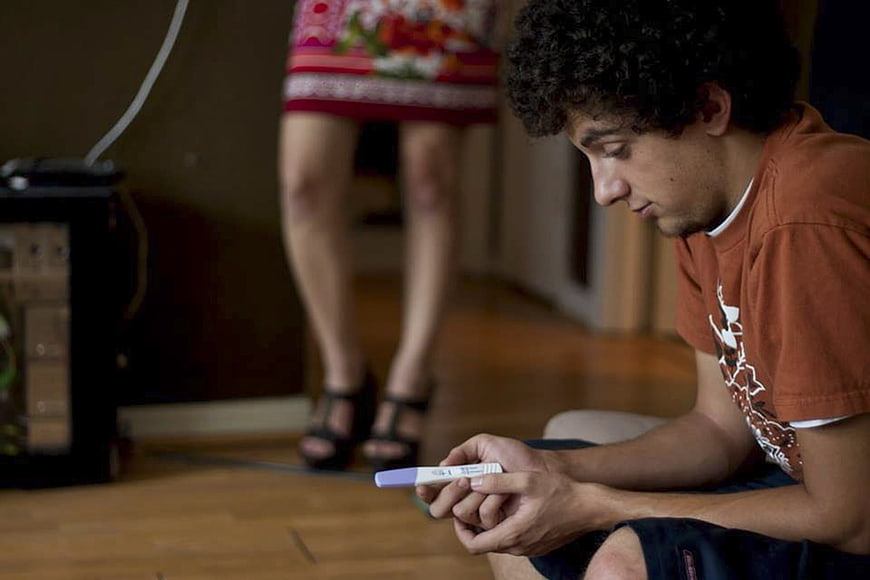 Young Man Holding Pregnancy Test with Woman Standing in Background