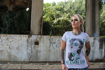 Tattooed woman with dreadlocks standing by graffiti wall