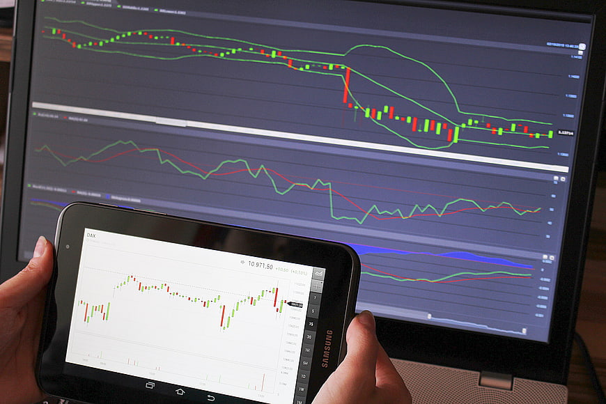 Hands holding Samsung tablet displaying DAX stock chart in front of laptop monitor