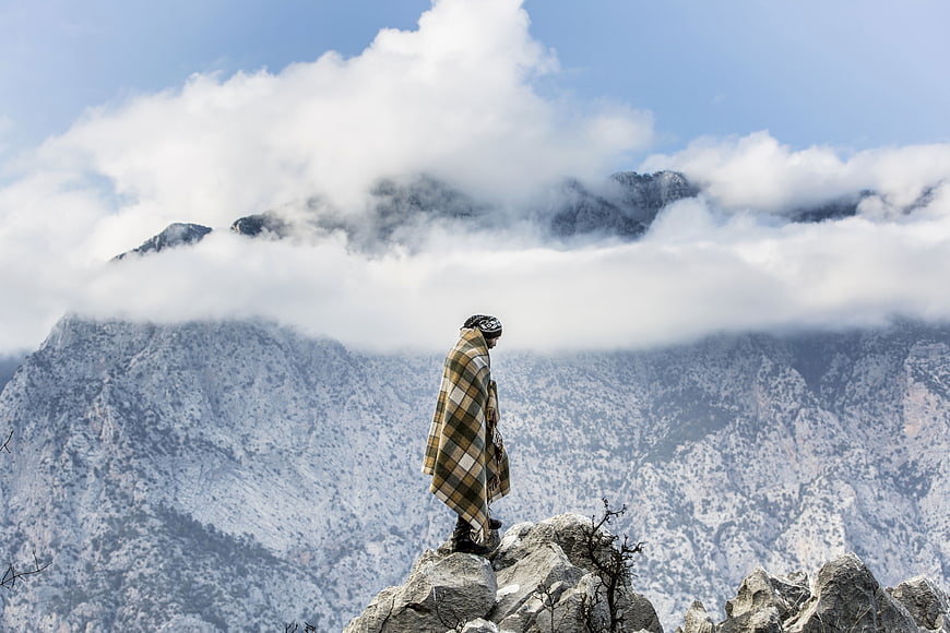 Man in Plaid Blanket Standing on Snowy Mountain Peak