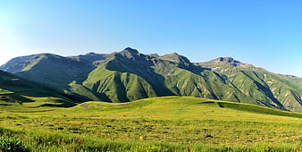 Lush Green Mountain Landscape With Blue Sky And Rolling Pastures