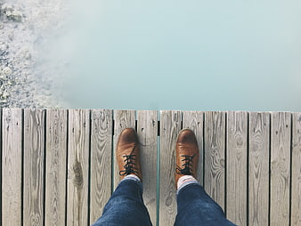 First-person view of brown boots on wooden dock over water