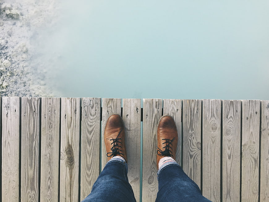 First-person view of brown boots on wooden dock over water